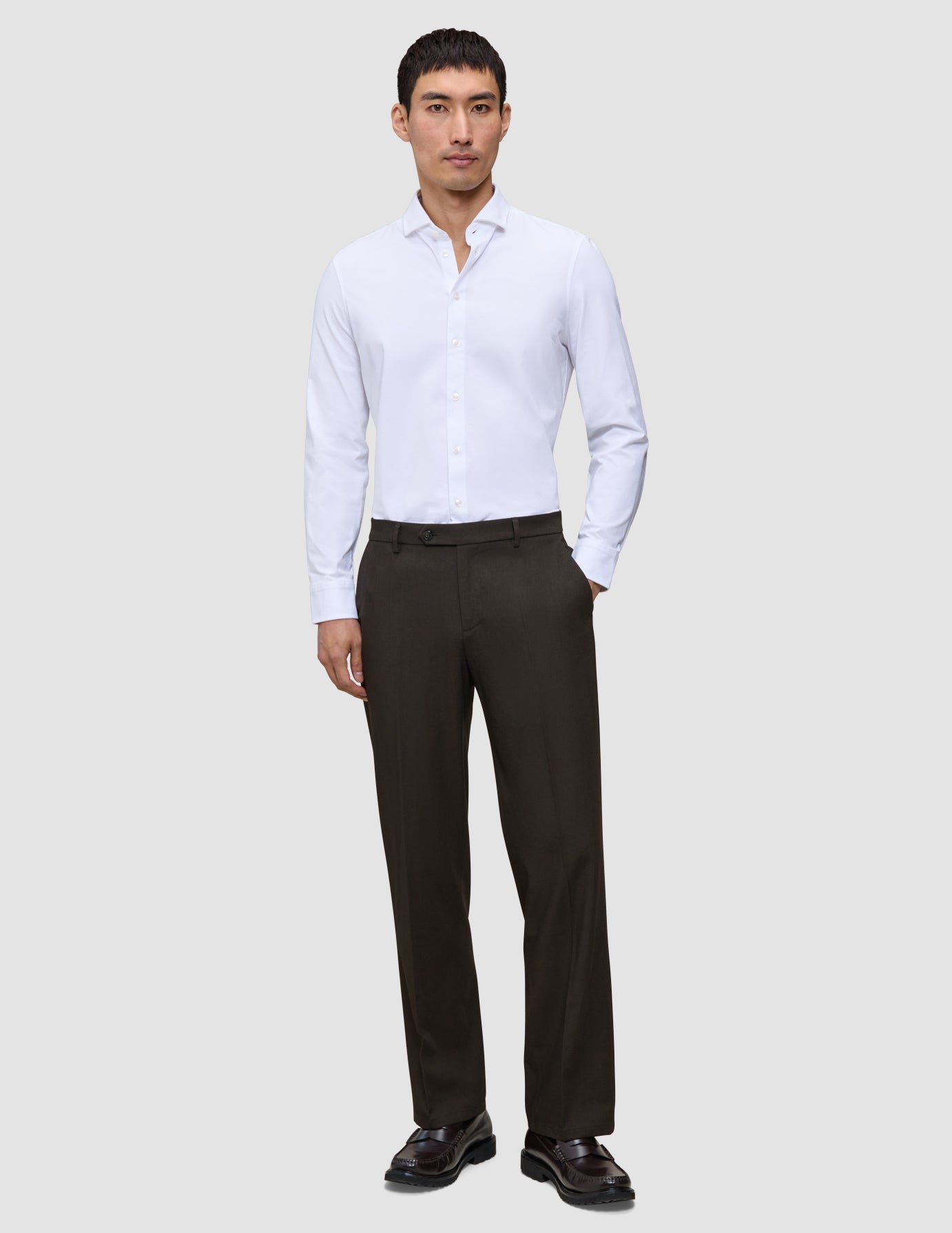 A man wears a white button-down shirt with a relaxed fit, Motion Suit Pants Relaxed Cognac, and dark loafers.