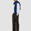 A man wearing a white pinstriped button-down shirt, a navy blue sweater draped over his shoulders, loafers, and Motion Suit Pants Relaxed Cognac.