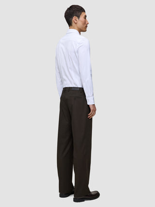 A man viewed from behind wears a white button-down shirt, Motion Suit Pants Relaxed Cognac, and dark brown loafers.