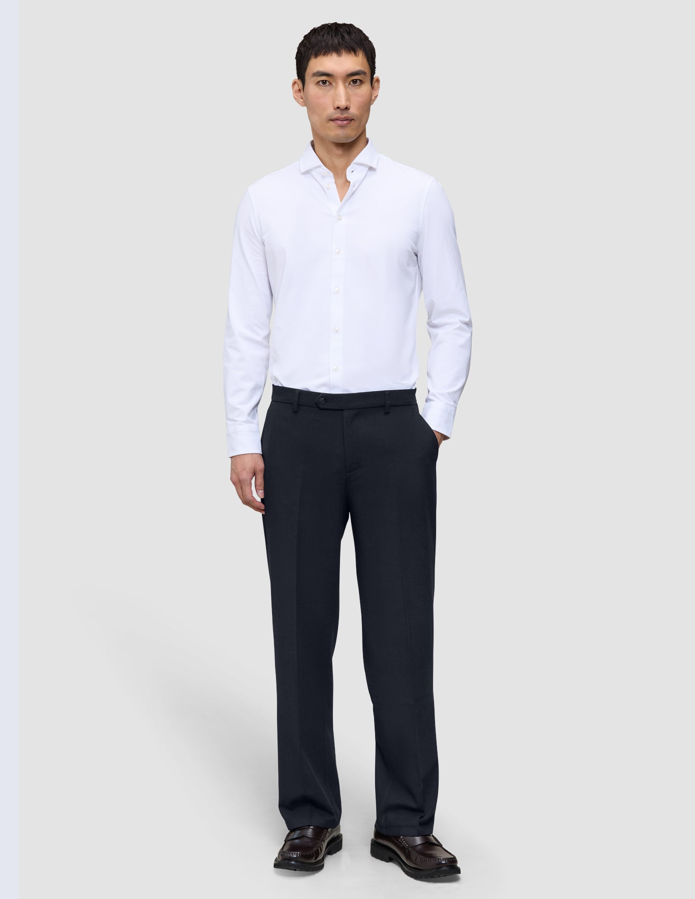 A man wearing a white button-down shirt and Motion Suit Pants Relaxed Midnight Blue, standing with one hand in his pocket.
