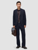 A man holding a brown leather briefcase, wearing a dark blue suit jacket, a dark brown button-down shirt, dark loafers, and Motion Suit Pants Relaxed Midnight Blue.