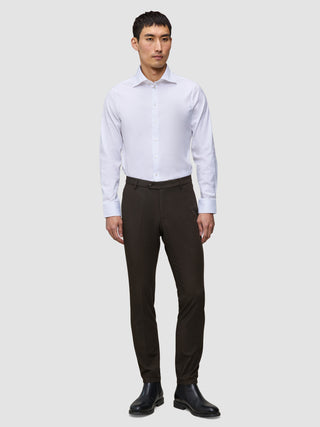 A man wears a white button-down shirt, black leather boots, and slim-fit dark brown Motion Suit Pants Slim Cognac.