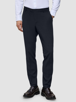 A person wearing a white button-down shirt, Motion Suit Pants Slim Midnight Blue, and dark leather loafers.