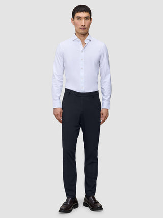 A man wears a white button-down shirt, Motion Suit Pants Slim Midnight Blue, and brown loafers.