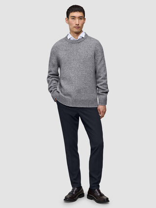 A man wearing a grey crew-neck sweater over a white collared shirt, paired with Motion Suit Pants Slim Midnight Blue and dark brown loafers.