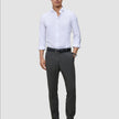 A man wearing a white button-down shirt, a black belt, and Motion Suit Pants Slim Pepper Grey made from breathable charcoal grey fabric.
