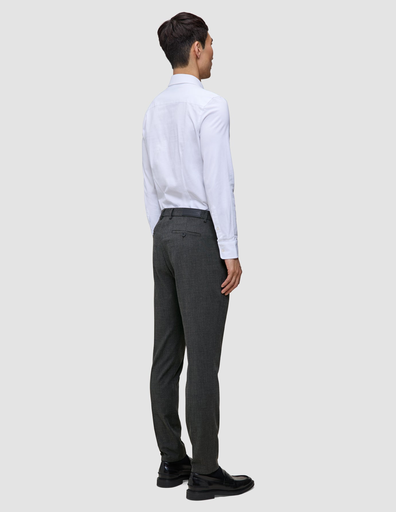 A man viewed from the back wearing a white button-down shirt and Motion Suit Pants Slim Pepper Grey with 360° stretch.
