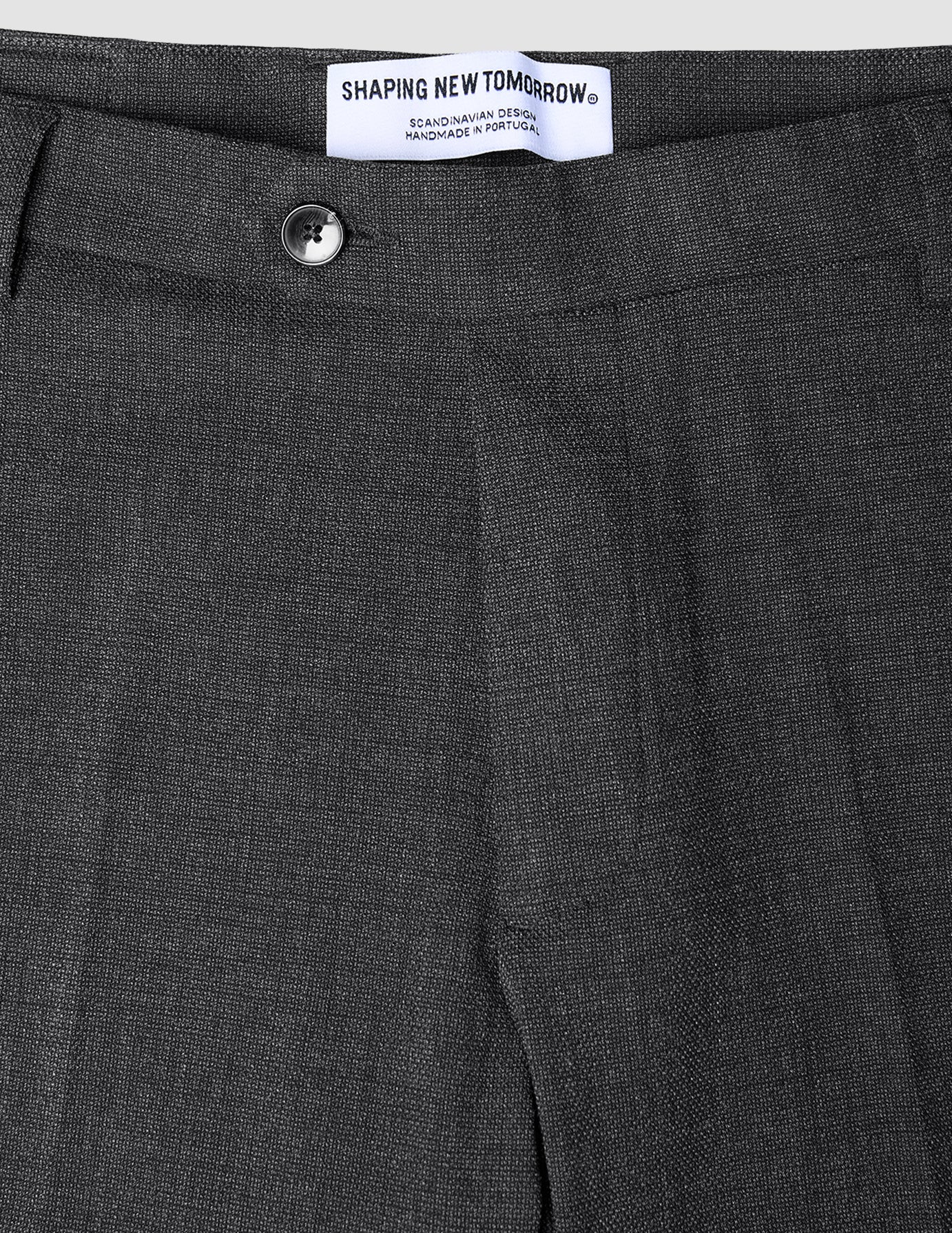 Close-up of the waistband and top of dark grey Motion Suit Pants Slim Pepper Grey, featuring a single button closure, 360° stretch slim-fit, and an interior brand label reading Shaping New Tomorrow.
