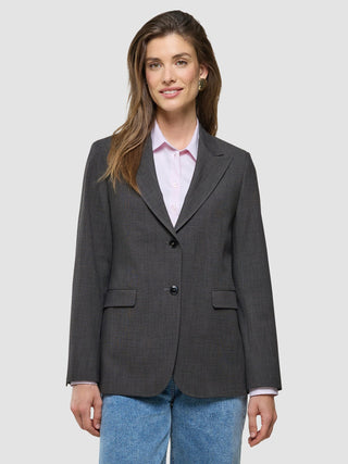 A smiling woman wearing a Women Nara Blazer Cool Brown over a light pink collared shirt and blue jeans.