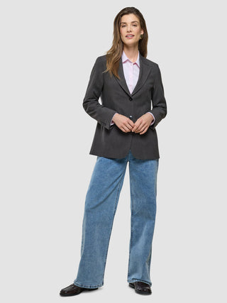 A woman wearing a Women Nara Blazer Cool Brown over a pale pink collared shirt and blue wide-leg jeans.