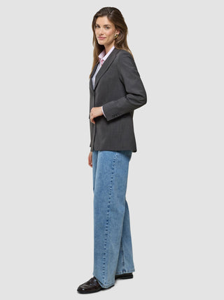 A woman standing in profile, wearing a Women Nara Blazer Cool Brown over a light pink button-down shirt and wide-leg blue jeans.