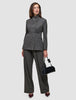 A woman wearing The suit with a statement in grey, featuring a high-neck jacket and matching wide-leg trousers, holding a small black handbag.
