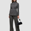 A woman wearing The suit with a statement in grey, featuring a high-neck jacket and matching wide-leg trousers, holding a small black handbag.