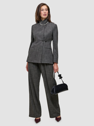 A woman wearing The suit with a statement in grey, featuring a high-neck jacket and matching wide-leg trousers, holding a small black handbag.