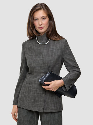 A woman wears The suit with a statement in grey plaid, featuring a blazer and matching wide-leg pants paired with a high-neck jacket, a single-strand pearl necklace, and a black clutch.