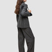 A person wearing The suit with a statement in a classic check pattern, featuring a Nara Blazer and wide-leg pants, while carrying a black shoulder bag.