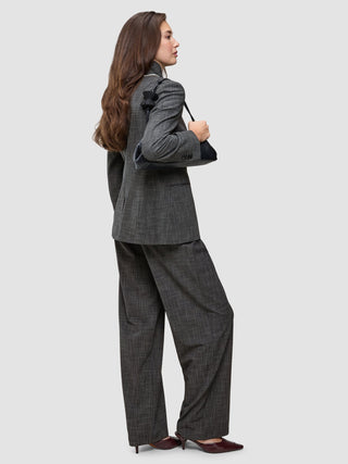 A person wearing The suit with a statement in a classic check pattern, featuring a Nara Blazer and wide-leg pants, while carrying a black shoulder bag.