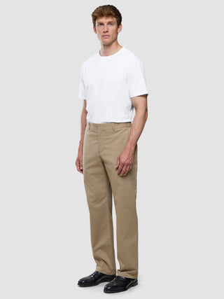 A man wearing a white crew-neck t-shirt, Refine Cotton Pants Relaxed Fit Sand, and black dress shoes.