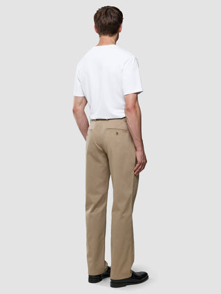 A man seen from behind wearing a white t-shirt, Refine Cotton Pants Relaxed Fit Sand, and black loafers.