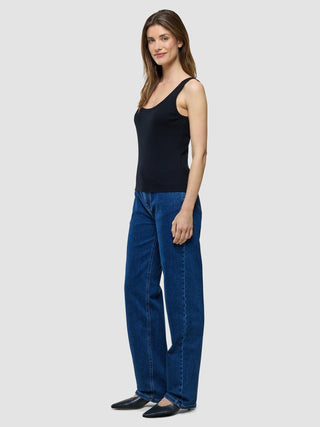 A woman wearing a Rib Tank Top Black and blue jeans stands in profile.