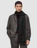 A person wearing a Scarf Black with tasseled ends over a black sweater and a brown jacket.