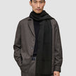 A person wearing a Scarf Black with tasseled ends over a black sweater and a brown jacket.