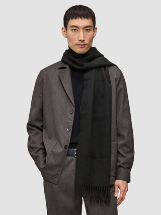 A person wearing a Scarf Black with tasseled ends over a black sweater and a brown jacket.