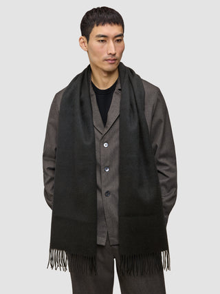 A person wearing a long, fringed Scarf Black over a dark jacket.