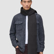 A man wears a Scarf Charcoal Grey with fringe ends over a white button-down shirt and a grey wool shirt jacket in a minimalist Scandinavian design.