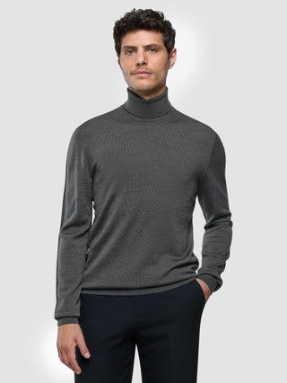A man wearing a Seamless Premium Merino Knit Turtleneck Charcoal Grey and dark trousers.
