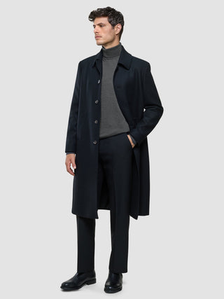 A man wearing a Seamless Premium Merino Knit Turtleneck Charcoal Grey, dark trousers, and a long dark overcoat.