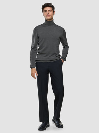 A man stands wearing a Seamless Premium Merino Knit Turtleneck Charcoal Grey, paired with dark trousers and black shoes.