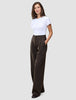 A woman stands wearing a white t-shirt and Serene Pants Wide Walnut Herringbone, which are dark, high-waisted wide-leg trousers with thin vertical pinstripes.