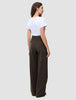 A woman wearing a white t-shirt and Serene Pants Wide Walnut Herringbone, high-waisted, dark brown, pinstriped, wide-leg trousers, viewed from the back.