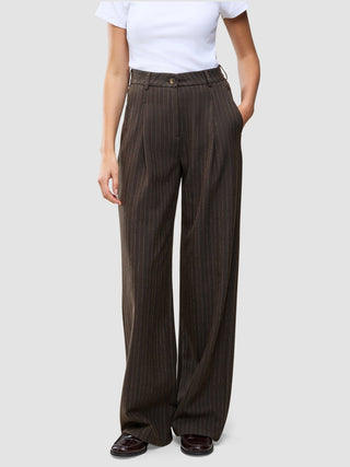 A person wearing Serene Pants Wide Walnut Herringbone in a dark brown pinstripe pattern with a white t-shirt, embodying a minimalist Scandinavian design aesthetic.