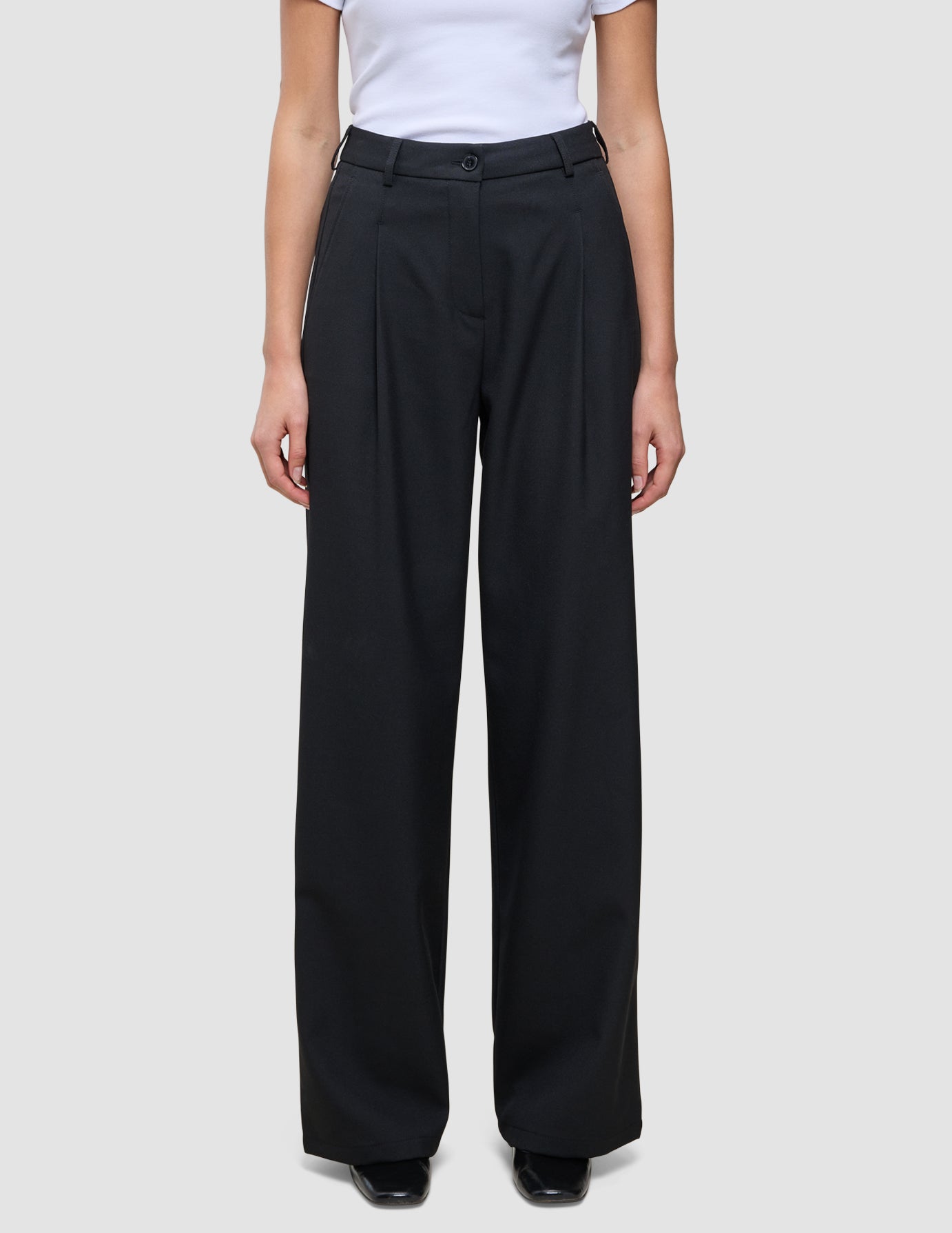 Serene Pants Wide Black featuring high-waisted black wide-leg trousers in a Scandinavian design with front pleats and a button closure.