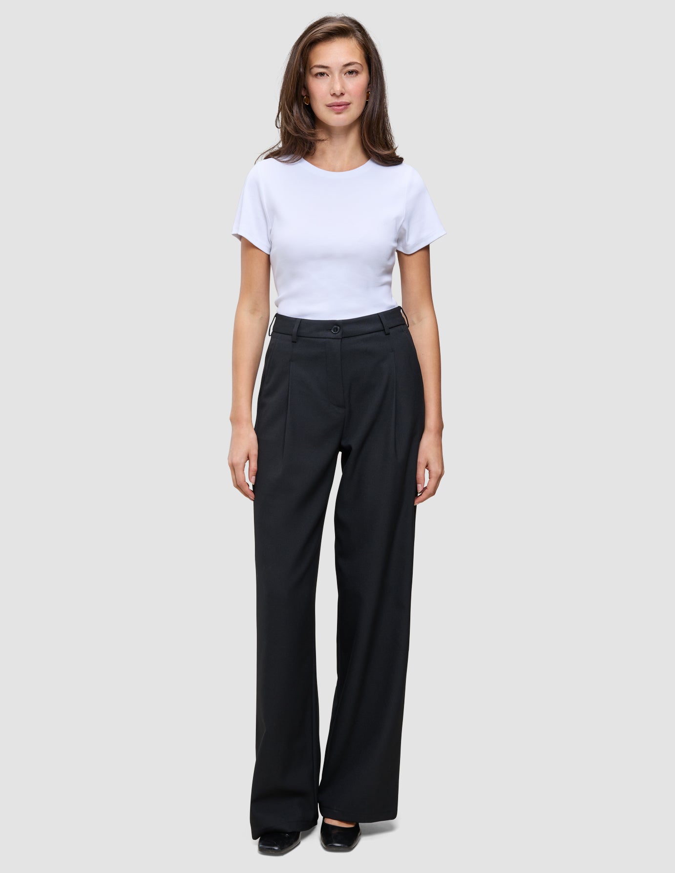A person wearing a white t-shirt and black Serene Pants Wide Black, featuring a high-waisted, wide-leg Scandinavian design.