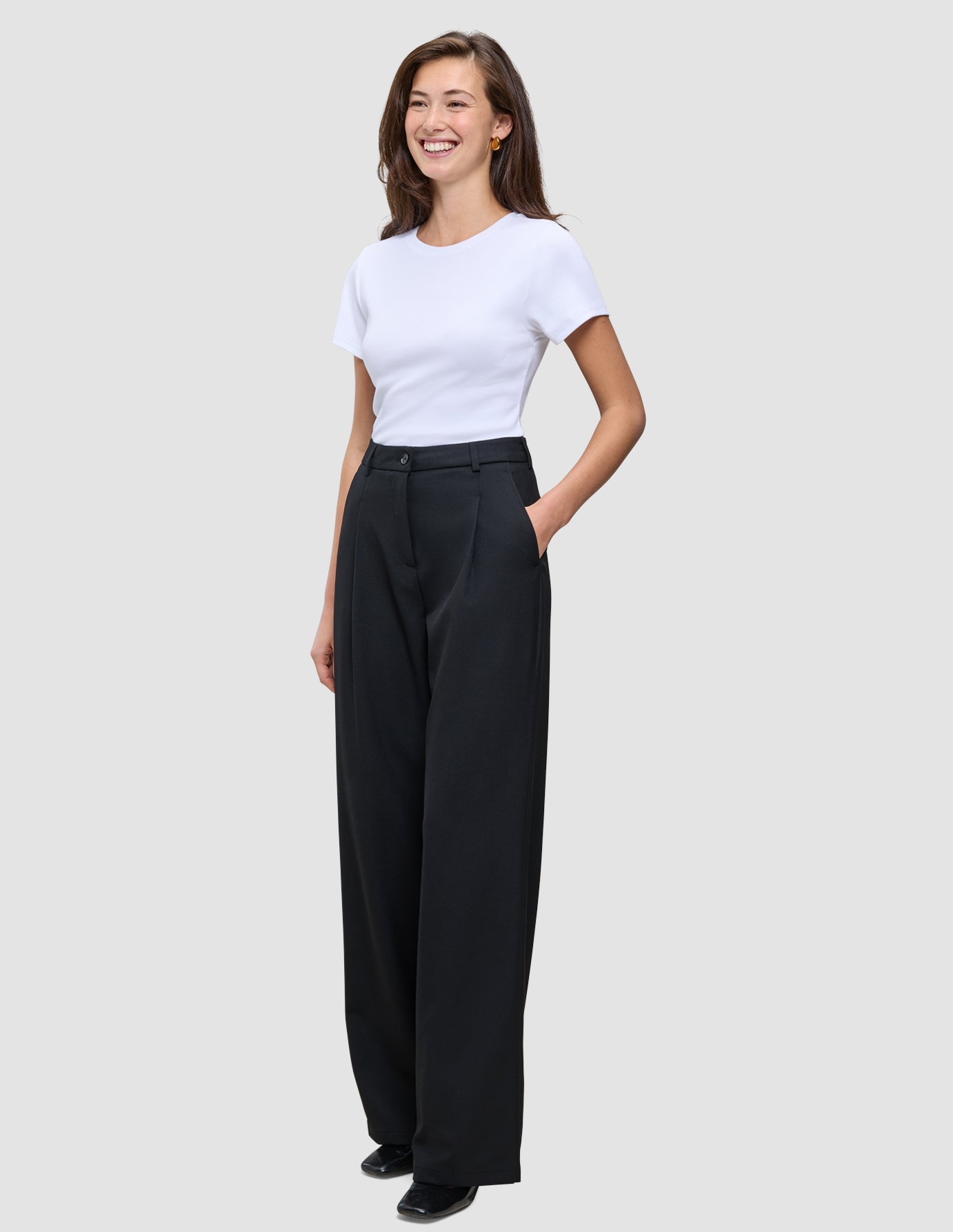 A smiling woman wears a white t-shirt tucked into high-waist, black Serene Pants Wide Black.