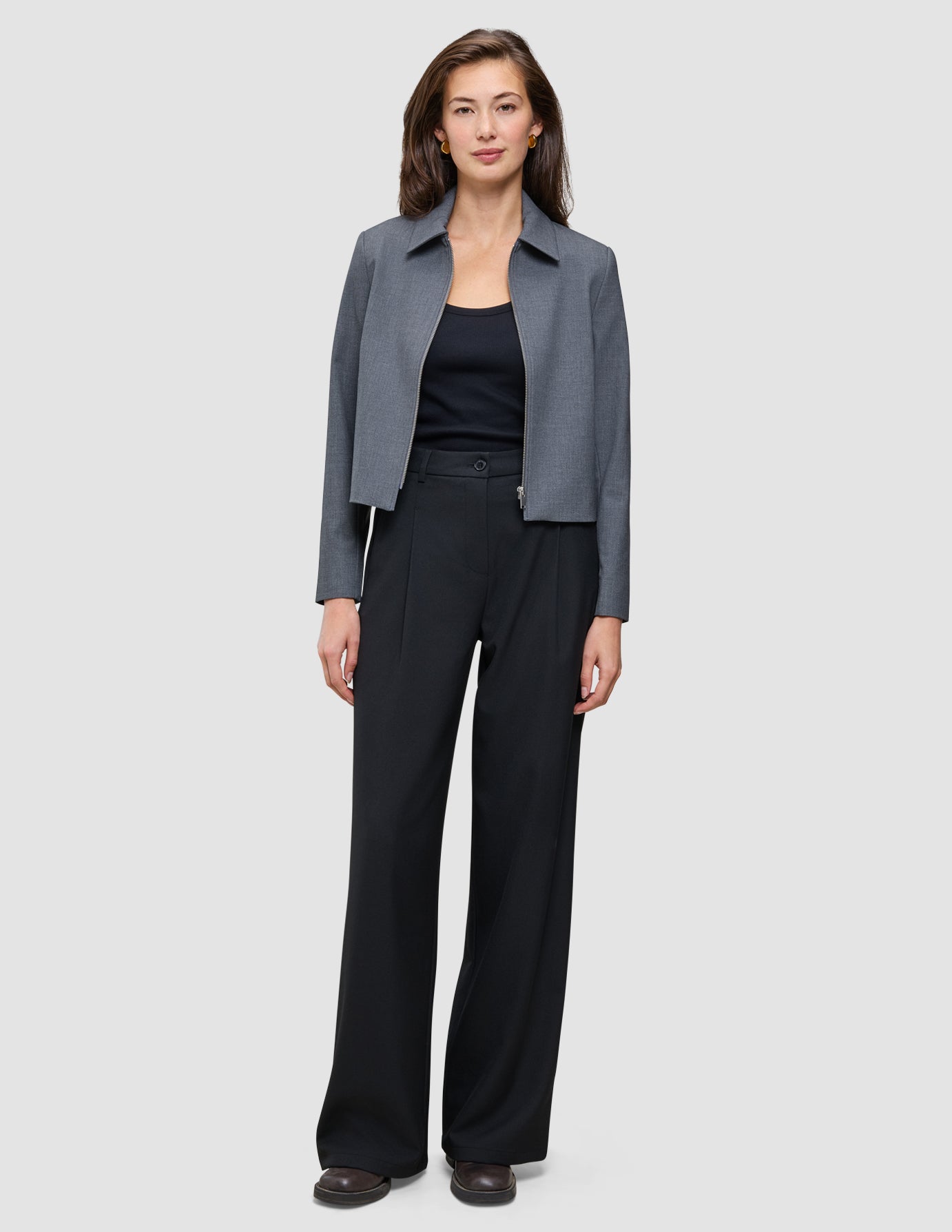 A woman wearing a grey zip-up jacket, a black tank top, and Serene Pants Wide Black.