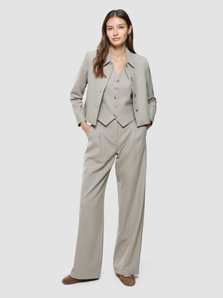 A woman wearing a matching light grey three-piece suit featuring the Women Serene Short Vest Burnt Sugar Herringbone.