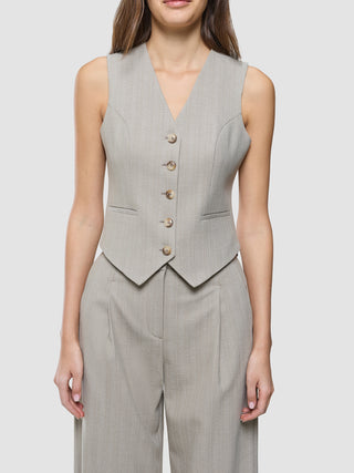 A woman wearing a Women Serene Short Vest Burnt Sugar Herringbone paired with matching trousers in a light gray pinstripe fabric.