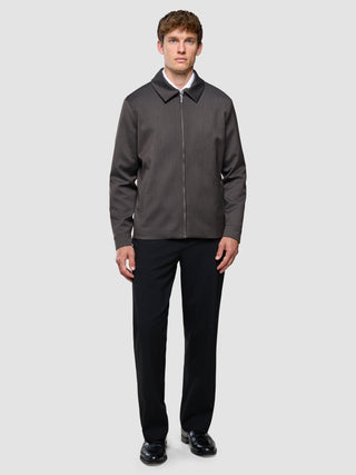 A man wearing a lightweight Siena Jacket Herringbone Dark Brown over a white shirt, paired with black trousers and black dress shoes.