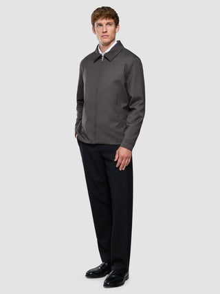 A man stands in a Siena Jacket Herringbone Dark Brown, wearing a white shirt and black trousers.