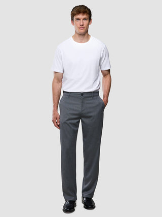 A man wearing a white crew-neck t-shirt, Siena Pants Relaxed Fit Herringbone Grey, and black dress shoes.