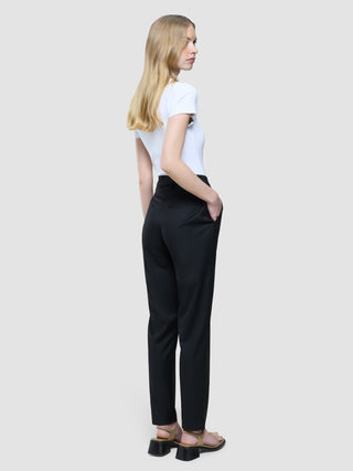 A woman from the back wearing a white t-shirt and Women Skye Pants Tapered Black with her hand in her pocket.