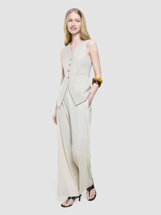 A woman wearing a Women’s Skye Long Vest Sandy Beige Melange and matching wide-leg trousers, accessorized with stacked bangles and black thong-strap heels.
