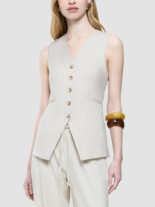 A person wears a Women’s Skye Long Vest Sandy Beige Melange over matching trousers, accessorized with two thick bangles on one arm.