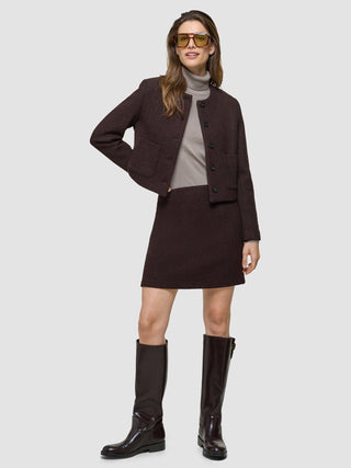 A model wears a brown tweed jacket and Women Sorae Short Skirt Espresso, a grey turtleneck, and knee-high boots.
