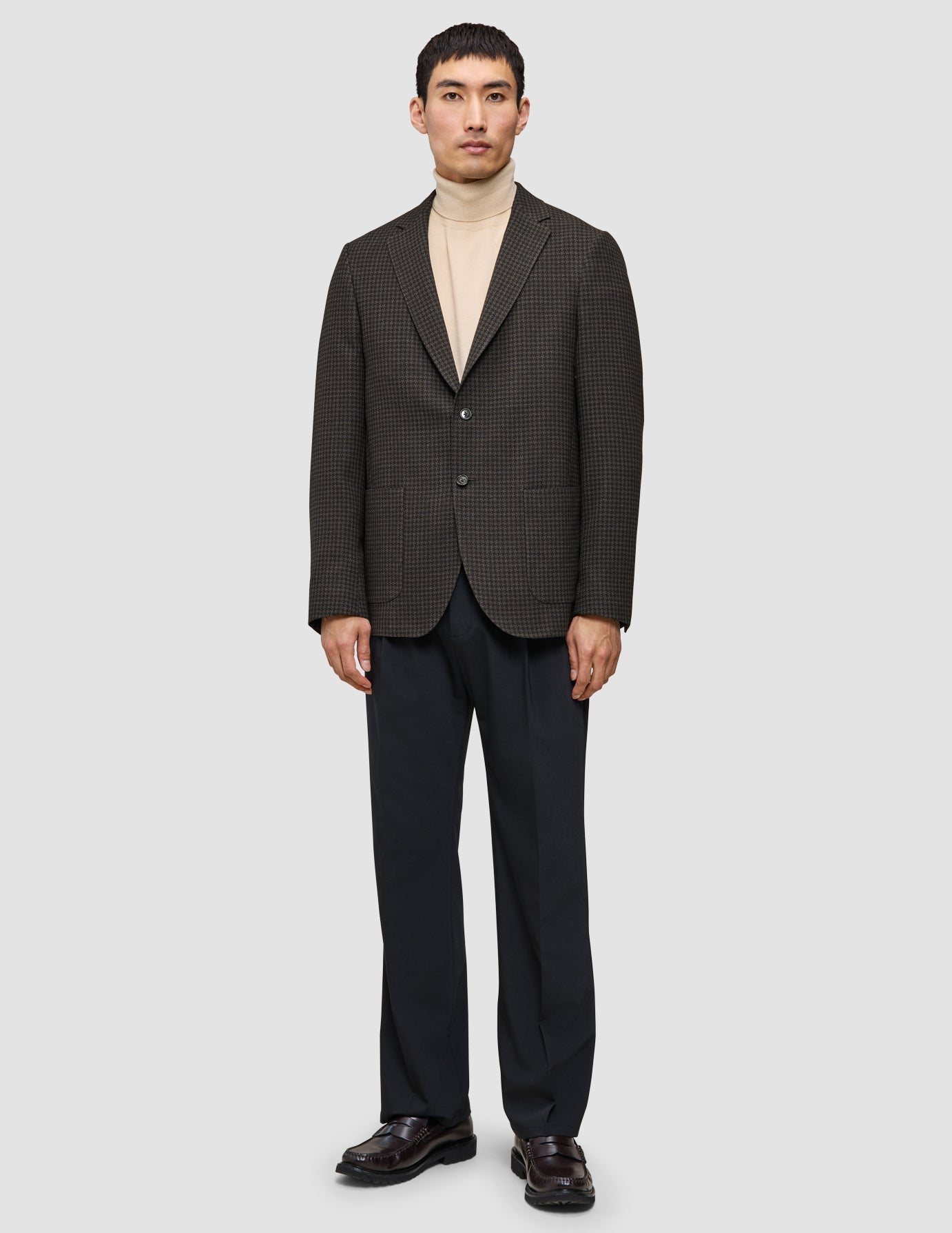A man wearing The knit-and-blazer look consisting of a tan merino crewneck under a dark patterned wool blazer with dark trousers and brown loafers.