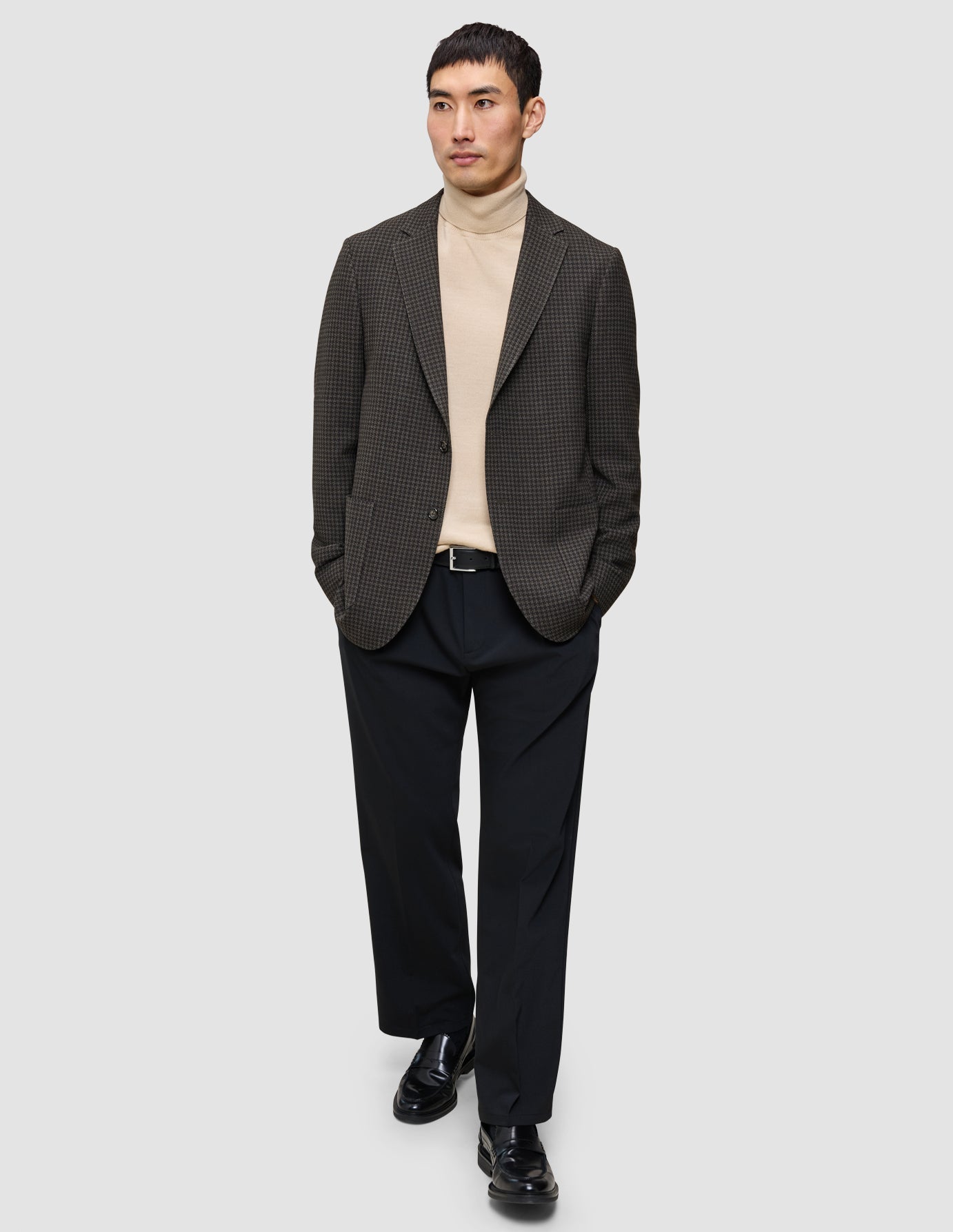 A man wearing The knit-and-blazer look consisting of a merino crewneck, a dark patterned wool blazer, and dark trousers.